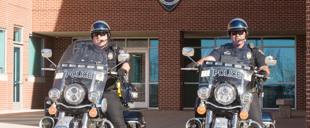 Two police officers on motorcycles outside a police station