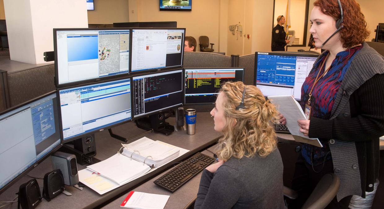 Two staff members overlook a call-center desk and monitors